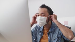 Asian young businessman working on computer in office with new normal lifestyle. Man wearing protective face mask to prevent covid virus after company reopen again. He put on mask and smile at camera. - Powered by Shutterstock - Get 15% off with code: PIKWIZARD15