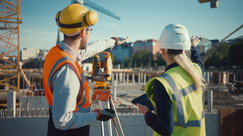 Construction Worker Using Theodolite Surveying Optical Instrument for Measuring Angles in Horizontal and Vertical Planes on Construction Site. Engineer and Architect Using Tablet Next to Surveyor. Royalty-Free Stock Footage #1057388128
