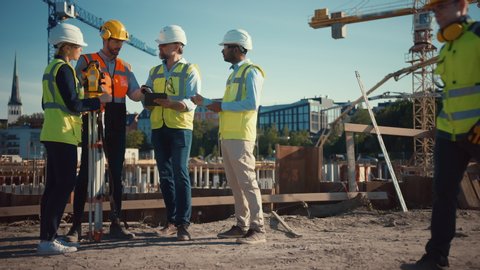 Diverse Team of Specialists Use Tablet Computer on Construction Site. Real Estate Building Project with Civil Engineer, Architect, Business Investor and Surveyor with Theodolite Discussing Plans.