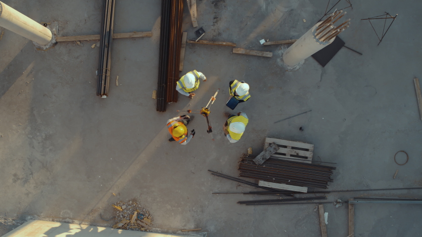 Aerial Top Down View on a Constructions Site with Diverse Team of Engineers and Worker with Theodolite Working. Heavy Machinery and Construction Workers in Hard Hats in the Area. Royalty-Free Stock Footage #1057388152