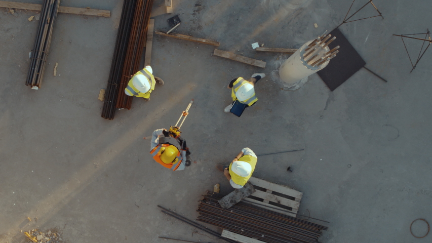Aerial Top Down View on a Constructions Site with Diverse Team of Engineers and Worker with Theodolite Looking Up and Smiling. Heavy Machinery and Construction Workers are Working in the Area. Royalty-Free Stock Footage #1057388185