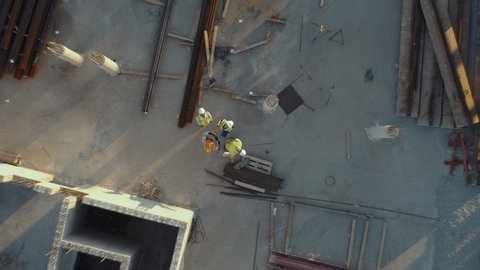 Aerial Top Down View on a Constructions Site with Diverse Team of Engineers and Worker with Theodolite Looking Up and Smiling. Heavy Machinery and Construction Workers are Working in the Area.