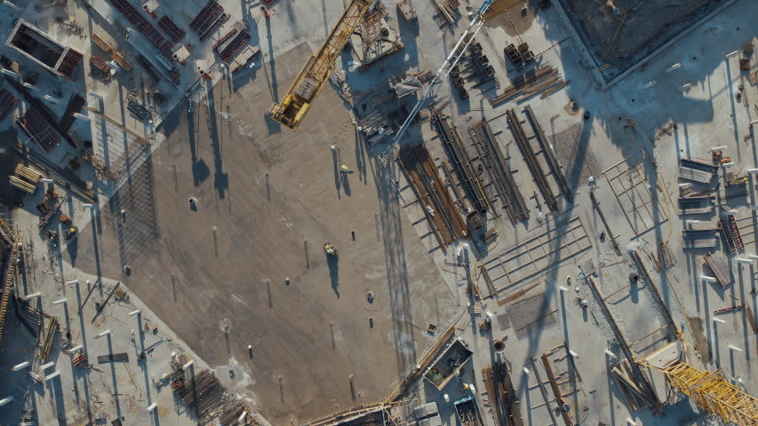 Aerial Flight Over a New Constructions Development Site with High Tower Cranes Building Real Estate. Heavy Machinery and Construction Workers are Employed. Top Down View at Contractors in Safety Hats. Royalty-Free Stock Footage #1057388203