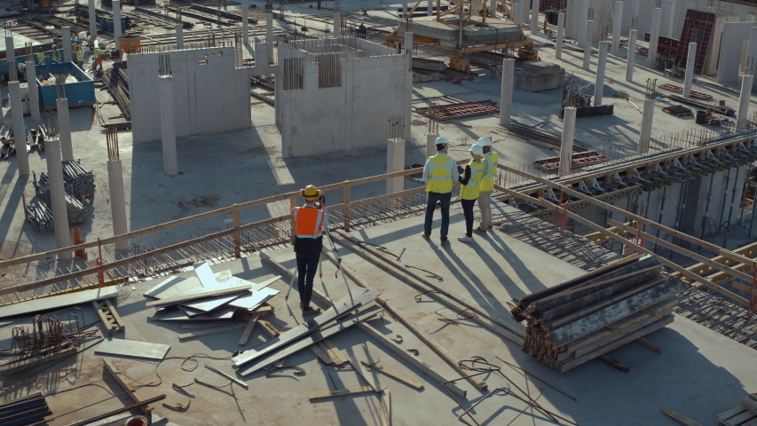 Aerial Flight Over a New Constructions Development Site with Diverse team of Engineers and Architects Discussing Real Estate Projects. Heavy Machinery and Construction Workers are Working in the Area. Royalty-Free Stock Footage #1057388230