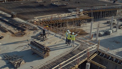 Aerial Flight Over a New Constructions Development Site with Diverse team of Engineers and Architects Discussing Real Estate Projects. Heavy Machinery and Construction Workers are Working in the Area.