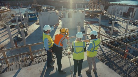 Construction Worker Using Theodolite Surveying Optical Instrument for Measuring Angles in Horizontal and Vertical Planes on Construction Site. Engineers and Architect Discuss Plans Next to Surveyor.