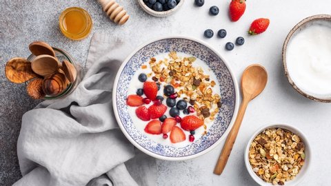 Stop motion animation of yogurt with granola and berries. Eating greek yogurt with crunchy oat honey granola, blueberries, strawberries and pomegranate seeds. Healthy food, healthy breakfast concept