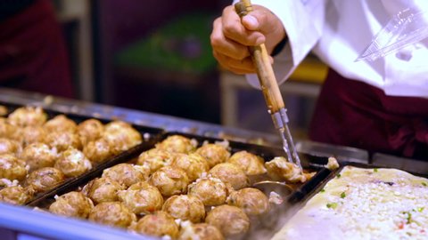 Chef hand pick up Japanese snack food takoyaki from takoyaki pan into the box for selling in summer festival at street food market in Japan. Man cooking assorted traditional Japanese meat ball.