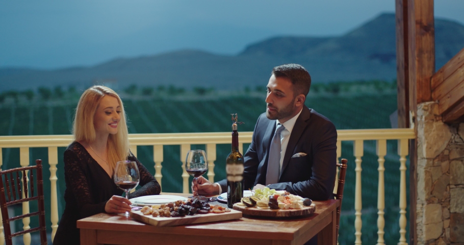 Young couple dining exclusively in a romantic atmosphere in restaurant . Pair enjoying romantic dinner in terrace near the vineyard . Couple drinking wine and making toast . Slow Motion . Royalty-Free Stock Footage #1057391092