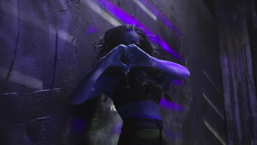Stylish brunette girl in sunglasses dancing near the wall with jalousie lines light . Trendy young woman dancing single in club . Hot girl with long hair performs modern dance against concrete wall .
