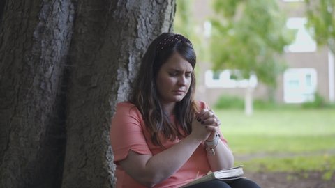 Portrait of a Woman Sitting by a tree praying with the Bible on her lap