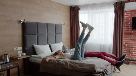 Slow motion of young happy woman and man going into hotel room and falling in bed laughing enjoying relaxation. Couple, fun and vacation concept.