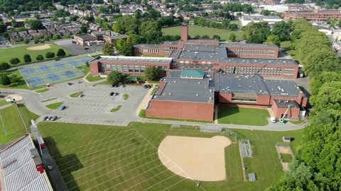 High aerial establishing shot of school, university, college campus with brick academic buildings and sports fields, tennis courts