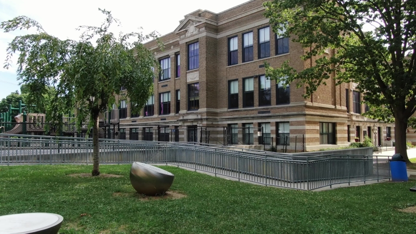 Rising aerial reveals American city school built in early 1900s, recess playground visible