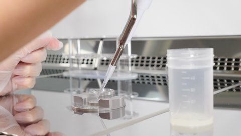 Close-up of doctor working with semen sample. scientist embryologist dispensing sperm out of test bank for analysis. Laboratory worker in modern microbiology cabinet.