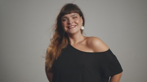 Beautiful plus size woman in black dress posing isolated on grey background. Plump happy female smiling at camera. Body positive concept