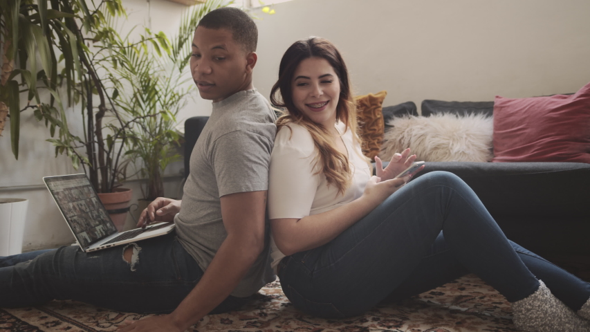 Interracial couple in love sitting on the carpet in the living room playing with each other back to back