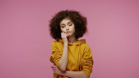 Lazy sleepy girl afro hairstyle in hoodie standing leaning on hand, looking at camera with bored indifferent expression, exhausted of tedious communication. studio shot isolated on pink background