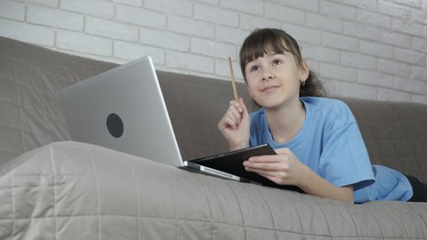 Teen go to school from home. A happy child solve her homework by the computer in the bed.