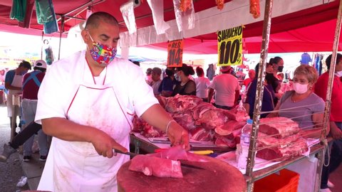 MEXICO CITY, AUG 2020. Butcher wearing face mask cuts some pieces of meat in a street market, clients await. Local authorities decreased measures about the COVID-19. Some people wear face masks.