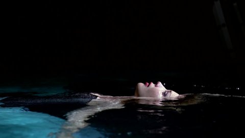 beautiful woman is floating in pool face up in night, dressed in gown