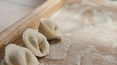 The national Russian dish of dumplings made of dough and meat. Close-up: on the wooden tray put the finished cake mix. Handicraft, home cooking, traditional national cuisine. Pelmeni