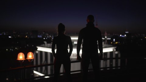 Silhouettes of national security agents looking at night cityscape from rooftop