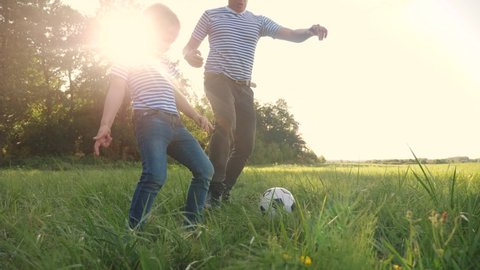 father and son playing football soccer in the park on the grass. happy family dream kid concept. dad and boy play ball outdoor sports in the park lifestyle healthy. parent plays with son into ball
