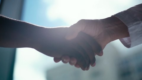 Close-up handshaking of two colleagues African business man and Caucasian businessman background of window, sunlight. Tracking shot in slow motion. Concept of interracial friendship and cooperation.