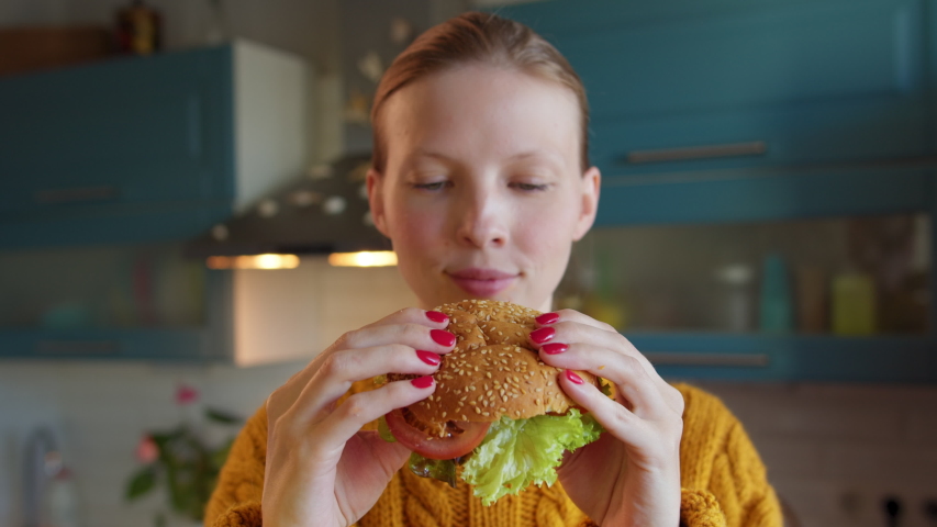 Close-up funny face young woman eating burger at home kitchen. Funny emotions, homemade vegetarian Burger. Healthy lifestyle | Shutterstock HD Video #1057413355