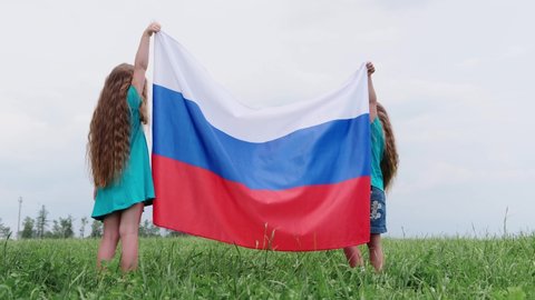 4k. Two girl sisters having fun waving national Russia flag outdoors running on green grass at summer - russian flag, country, patriotism, Russia day.