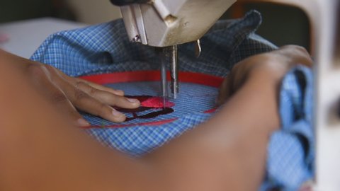 A woman using a sewing machine to embroider a flower onto an apron in Oaxaca, Mexico. Slow-motion, close-up of her hands and arms.