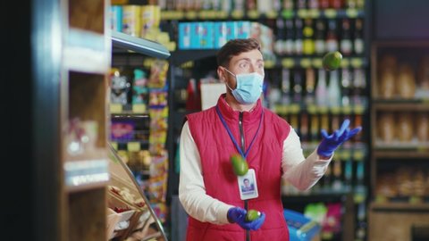 Funny young seller man with mask juggling fruit in supermarket vegetable business beautiful fresh produce retail shop slow motion