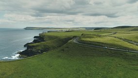 Green fields, meadows aerial: road cars driving on background. Ireland's hills, farmlands, clouds on horizon. Picturesque landscape view of Antrim County, United Kingdom. Footage shot in 4K, UHD