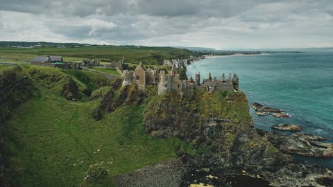 Irish castle cliff shore aerial view: Dunluce on green grass valleys and meadows overlooking ocean bay. Beautiful stones and reefs. Beauty of Northern Ireland's historic ruins. Footage shot in 4K, UHD