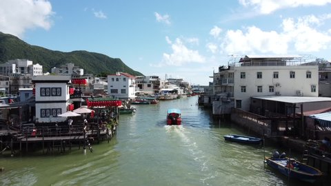 Aerial of Touristic Boat Sailing in Canal of Tai O Fishing Village, Hong Kong. Picturesque Island and Stilt Houses Under Beautiful Sky, Drone Shot