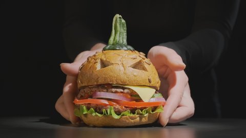 Female hands of waiter serve beef burger in image of pumpkin for Halloween on black background. halloween party dish
