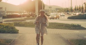 Happy blonde woman in helmet rides scooter around the city at sunset. Move even faster thanks to scooters. 4K video Slow motion. 