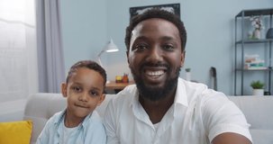 POV of happy African American handsome male with little son waving their hands while videochatting on smartphone at home. Joyful father and cute kid boy having video call on cellphone. Leisure concept