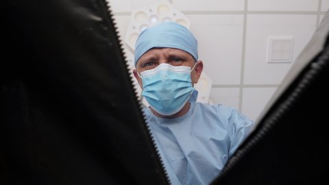 The pathologist opens a plastic bag with a dead body inside the hospital morgue. A corpse in a black plastic bag. First-person view, conceptual footage