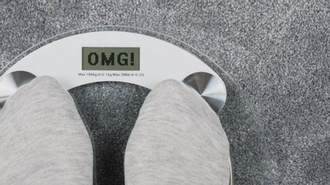 Overweight on bathroom scales. OMG inscription on digital display. Health and personal care concept. A person steps on the scales to check her weight. First-person view