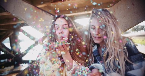 Close up young blonde women blowing colorful confetti by pier