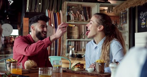 Young middle-eastern man feeding frie to blonde friend at restaurant
