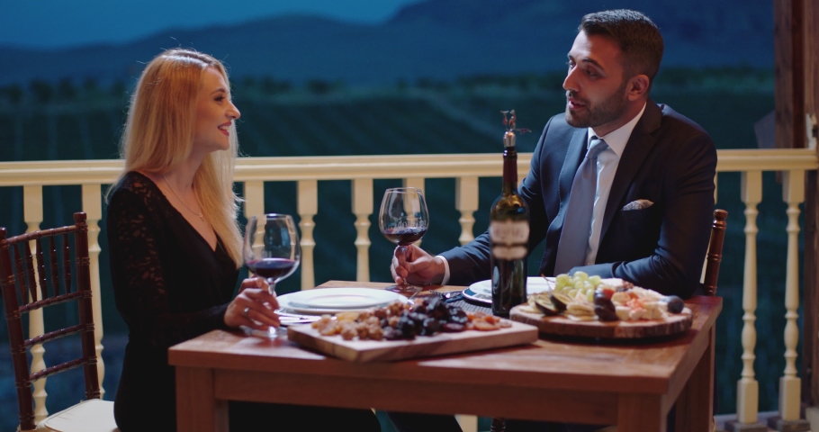 Young couple dining exclusively in a romantic atmosphere in restaurant . Pair enjoying romantic dinner in terrace near the vineyard . Couple drinking wine and making toast . Slow Motion . Royalty-Free Stock Footage #1057441639