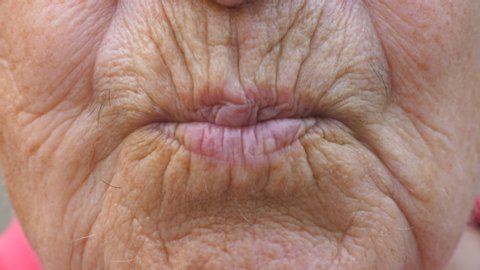 Close up lips of mature grandmother. Mouth of elder grandma sends air kiss into camera. Senior woman with wrinkled skin does kissing gesture. Slow motion