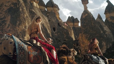 Amazing beautiful young blonde traveller tourist girl riding a cute camel in magical cappadocia and touring . A charming place in Turkey.