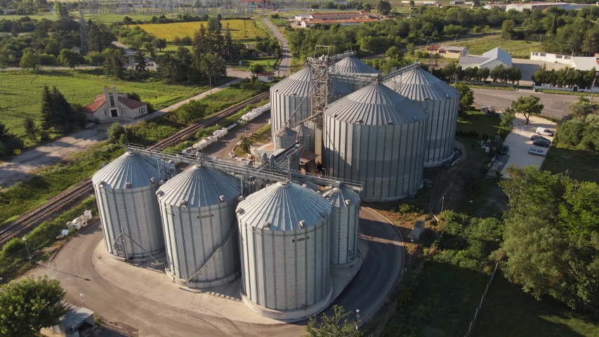 Farm Grain Storage Bins wheat field at sunset from top aerial view. Steel Granary storage tanks steel warehouse granary for storage of loose grain blue sky volumetric clouds. Elevator. Parked trucks.