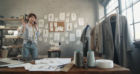 An asian female clothes designer working at her office, dialing or recording voice message for customer, making an order - small business concept 4k footage
