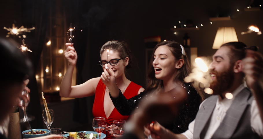 Group of multiethnic friends celebrating christmas together, cheering, smiling and holding burning sparklers at dinner party table - celebration, real people concept 4k footage | Shutterstock HD Video #1057452787