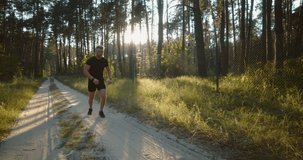 Full length portrait of young sportsman in black t-shirt and shorts doing evening cardio at green forest. Handsome man training on nature during amazing sunset.